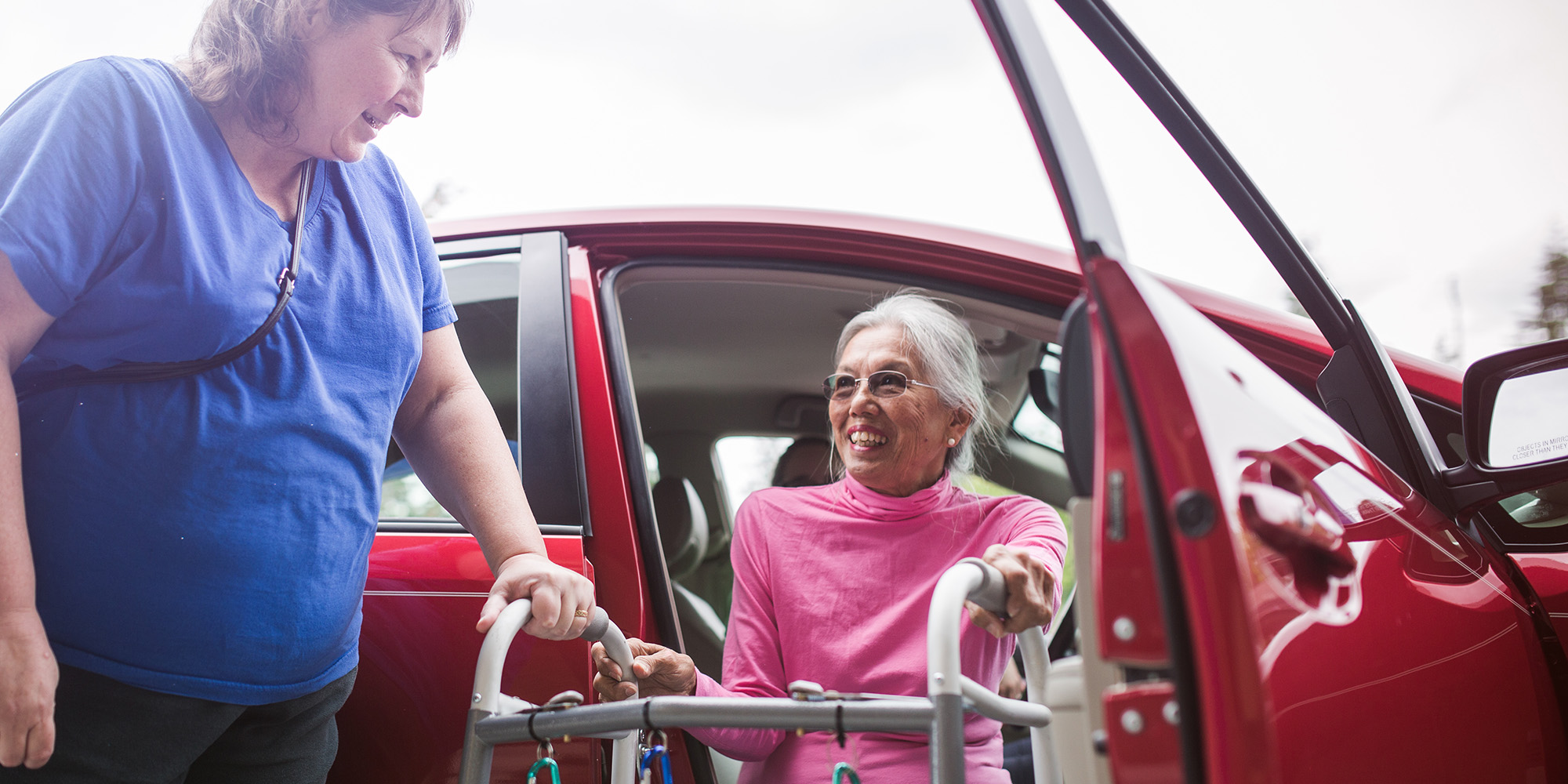 Woman receiving assistance getting out of a car with her walking device