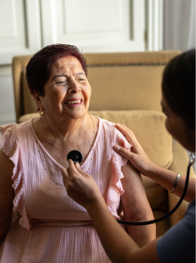 One woman smiles as another uses a stethoscope on her.